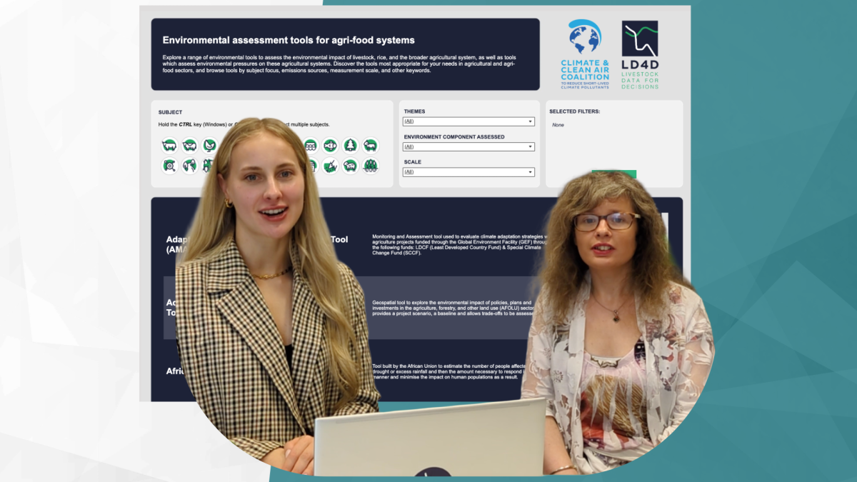 Two women sit at a laptop in front of a backdrop of a data dashboard