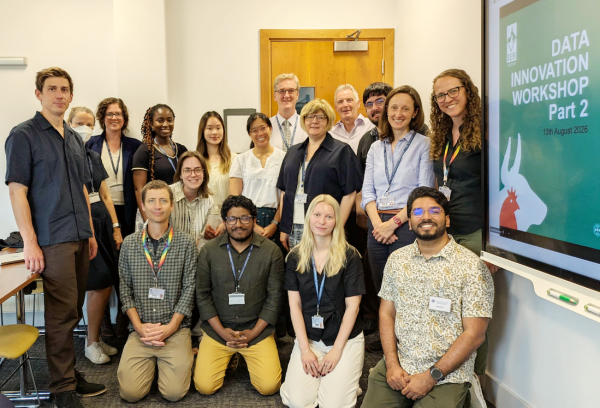 A group of people pose of mixed genders and ethnicities pose for a picture in a meeting room.